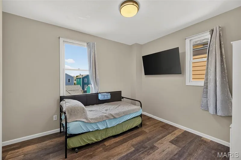 Bright secondary bedroom featuring wood-finish flooring, two windows with natural light, wall-mounted flat-screen television, and a ceiling-mounted light fixture — 3471 Hiram Street, St Charles, MO 63301