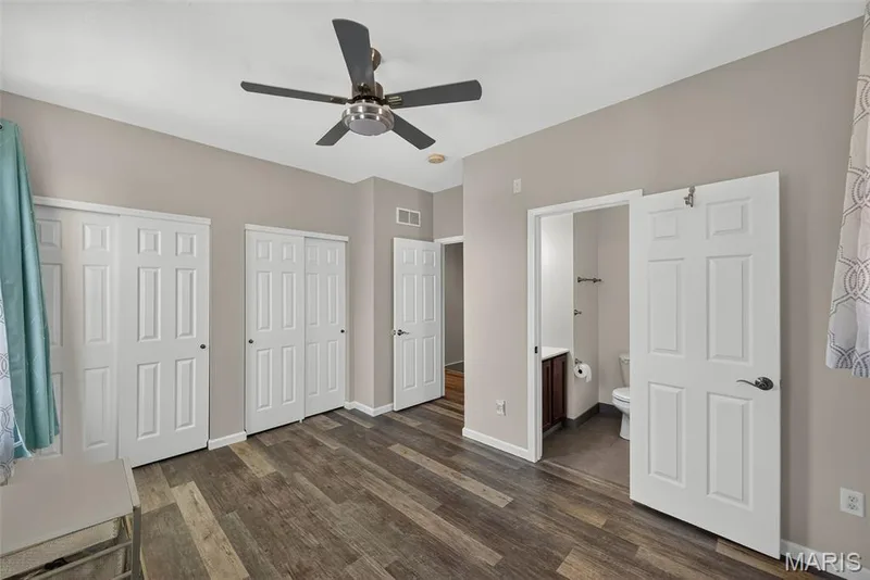 Spacious bedroom featuring multiple closet options with six-panel white doors, wood-finish flooring, ceiling fan with integrated lighting, and neutral wall finishes — 3471 Hiram Street, St Charles, MO 63301