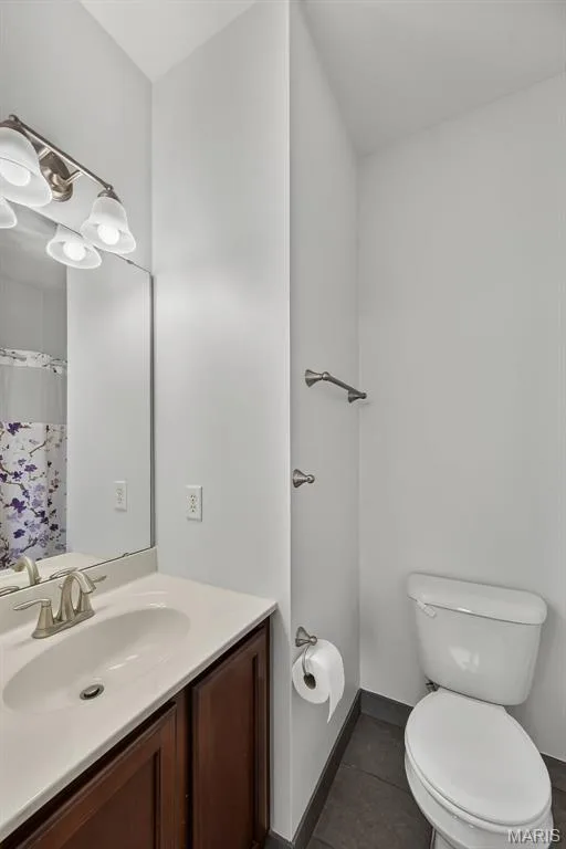 Modern bathroom featuring a wood-finish vanity with an undermount sink, brushed nickel faucet, and large illuminated mirror — 3471 Hiram Street, St Charles, MO 63301