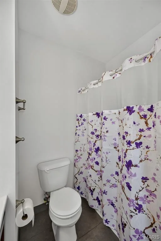 Functional bathroom featuring a standard toilet, ceramic fixtures, and decorative floral shower curtain with purple botanical print — 3471 Hiram Street, St Charles, MO 63301