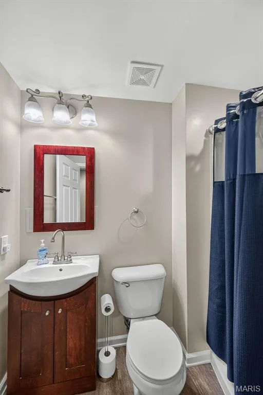 Bathroom featuring a wood-finish vanity with an integrated sink, a wall-mounted vanity light fixture, a toilet, a shower/tub combination, and wood-finish flooring — 3471 Hiram Street, St Charles, MO 63301