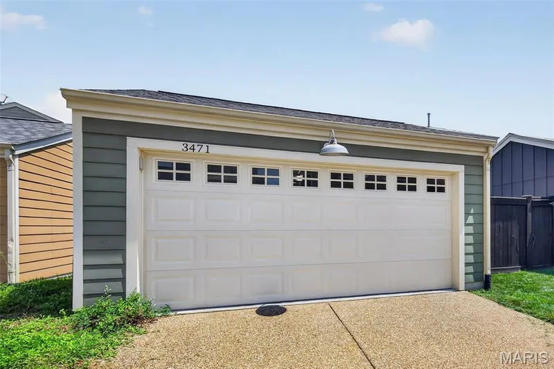 White paneled garage door with multiple horizontal sections and decorative hardware accents the front elevation of this residence — 3471 Hiram Street, St Charles, MO 63301