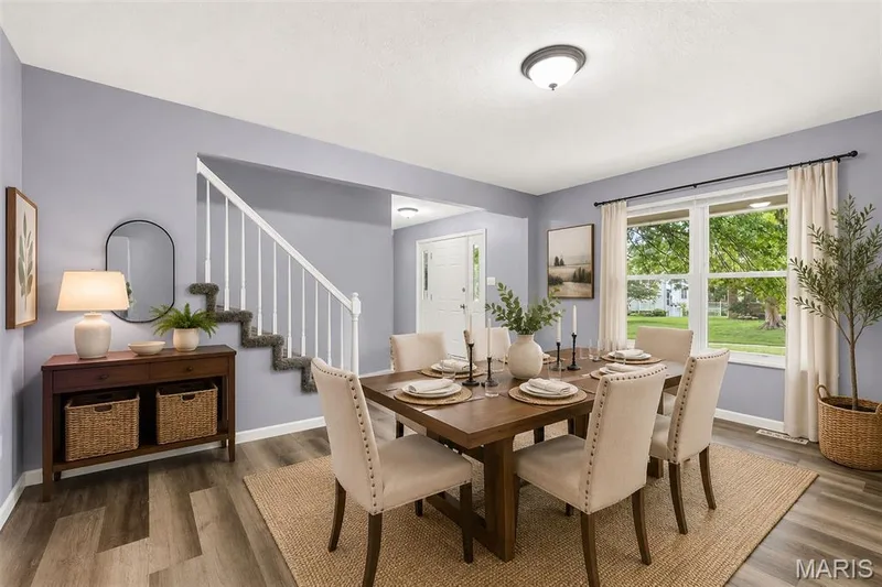 Spacious dining area featuring wood-finish flooring, a large window, a built-in ceiling light fixture, and a staircase with white spindles — 2947 Bromley Drive, O'Fallon, MO 63368