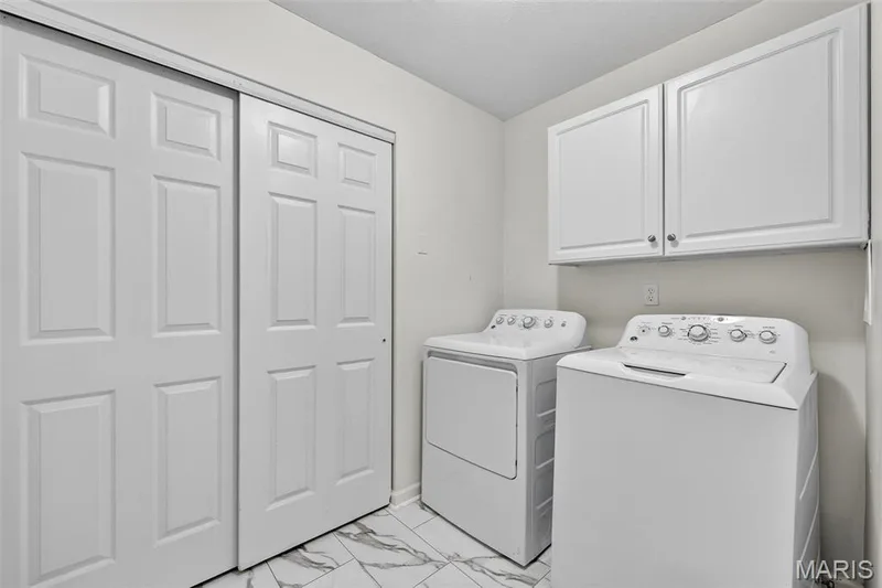 Laundry area featuring white cabinetry, white six-panel bifold doors, and patterned floor tile — 2947 Bromley Drive, O'Fallon, MO 63368