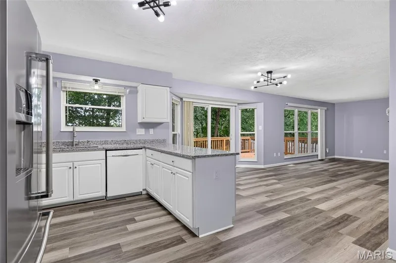 Open-concept living area featuring wood-finish flooring, a modern chandelier, and multiple sliding glass doors leading to exterior decking — 2947 Bromley Drive, O'Fallon, MO 63368