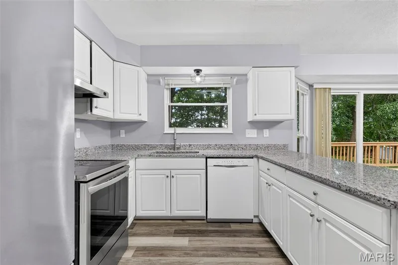 Kitchen featuring white cabinetry, light granite countertops, stainless steel appliances, and wood-finish flooring — 2947 Bromley Drive, O'Fallon, MO 63368