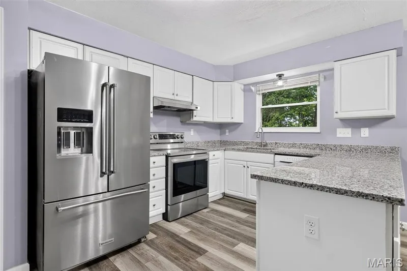 Kitchen featuring stainless steel appliances, white cabinetry, granite countertops, wood-finish flooring, and a large window — 2947 Bromley Drive, O'Fallon, MO 63368