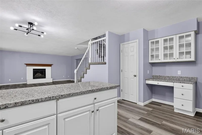 Open-concept living area with wood-finish flooring, a contemporary chandelier, and a white mantel fireplace — 2947 Bromley Drive, O'Fallon, MO 63368