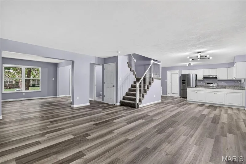 Open-concept living area featuring wood-finish flooring, a contemporary kitchen with white cabinetry and stainless steel appliances, a staircase with white balusters, and recessed window framing — 2947 Bromley Drive, O'Fallon, MO 63368