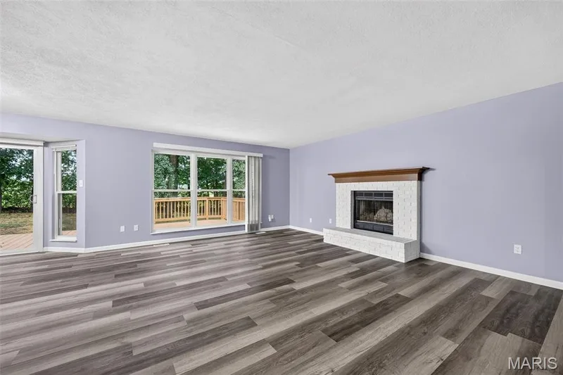 Spacious interior featuring wood-finish flooring, a white tiled fireplace with a wood mantle, and sliding glass doors to the exterior deck — 2947 Bromley Drive, O'Fallon, MO 63368