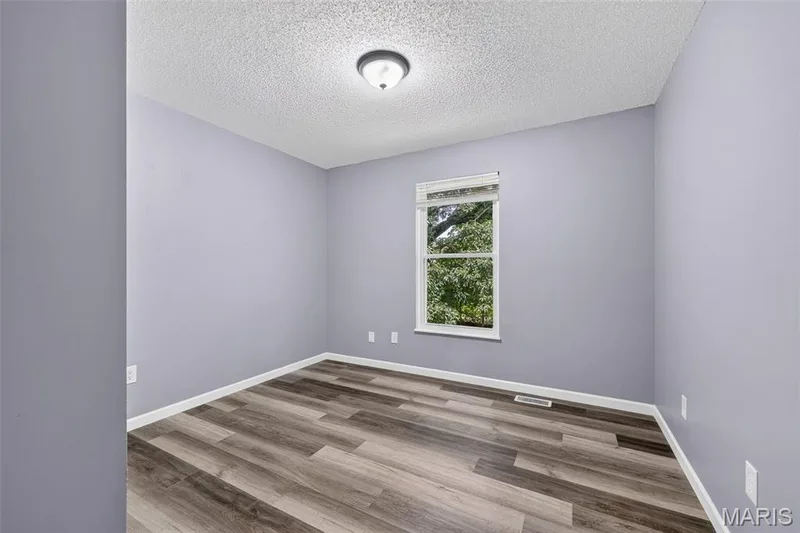 Spacious room featuring wood-finish flooring, light purple walls, and a white ceiling — 2947 Bromley Drive, O'Fallon, MO 63368