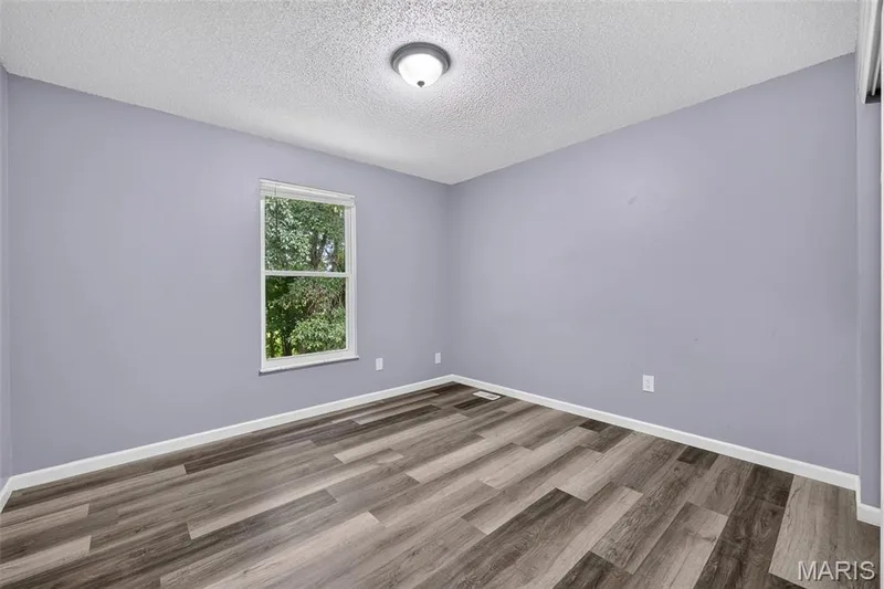 Interior room featuring wood-finish flooring, light purple walls, white baseboards, and a single window with white trim — 2947 Bromley Drive, O'Fallon, MO 63368
