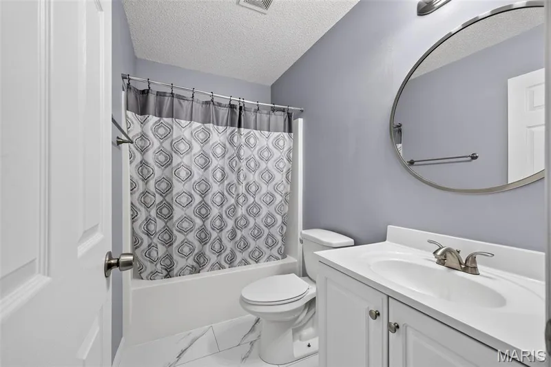 Bathroom featuring a white vanity with integrated sink, brushed nickel faucet, and a circular mirror — 2947 Bromley Drive, O'Fallon, MO 63368