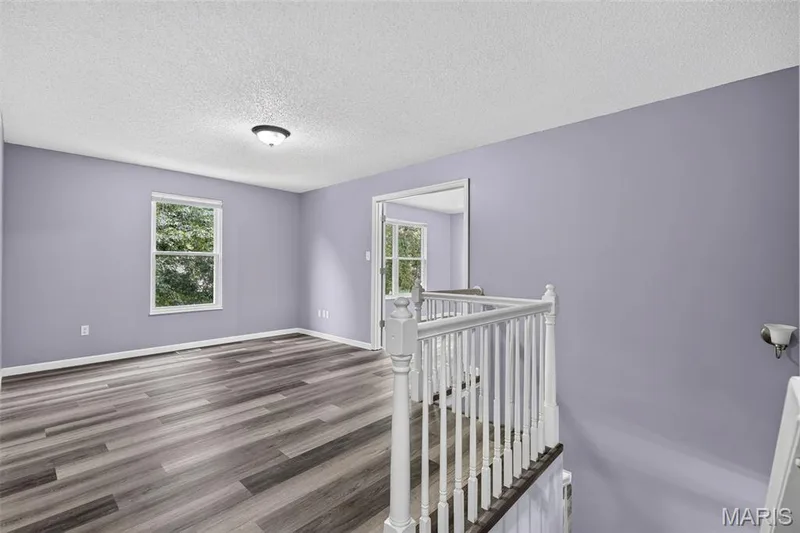 Loft area featuring wood-finish flooring, light purple wall paint, and white trim — 2947 Bromley Drive, O'Fallon, MO 63368