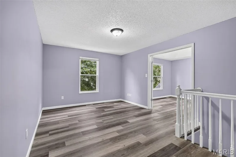 Upper-level landing featuring wood-finish flooring, light lavender walls, and a white baluster railing system — 2947 Bromley Drive, O'Fallon, MO 63368