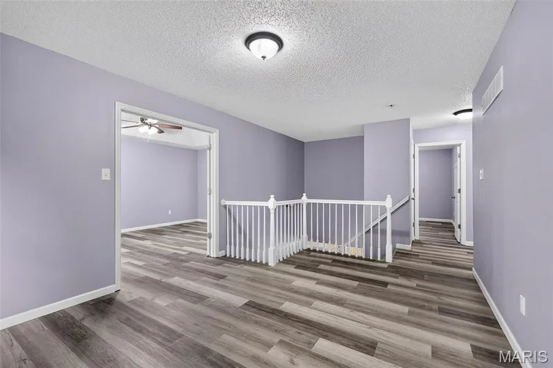 Interior space featuring wood-finish flooring, light purple wall paint, white trim, and a white staircase with balusters — 2947 Bromley Drive, O'Fallon, MO 63368