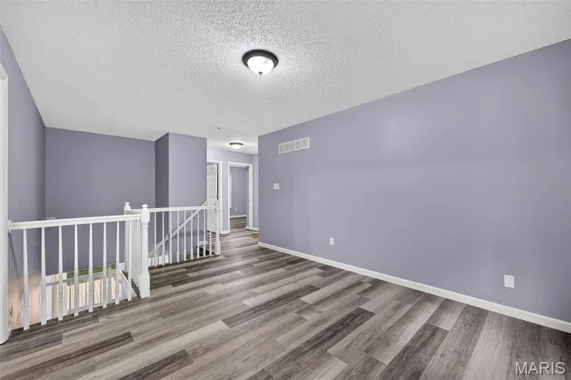 Expansive upper-level landing featuring wood-finish flooring, a white spindle railing, and overhead lighting — 2947 Bromley Drive, O'Fallon, MO 63368