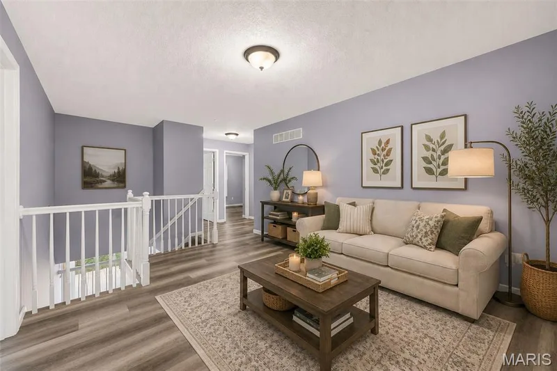 Open concept living space featuring wood-finish flooring, light purple wall tones, white trim, and a white staircase railing — 2947 Bromley Drive, O'Fallon, MO 63368
