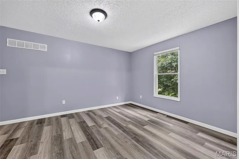 Room featuring wood-finish flooring, light purple wall paint, and white trim — 2947 Bromley Drive, O'Fallon, MO 63368