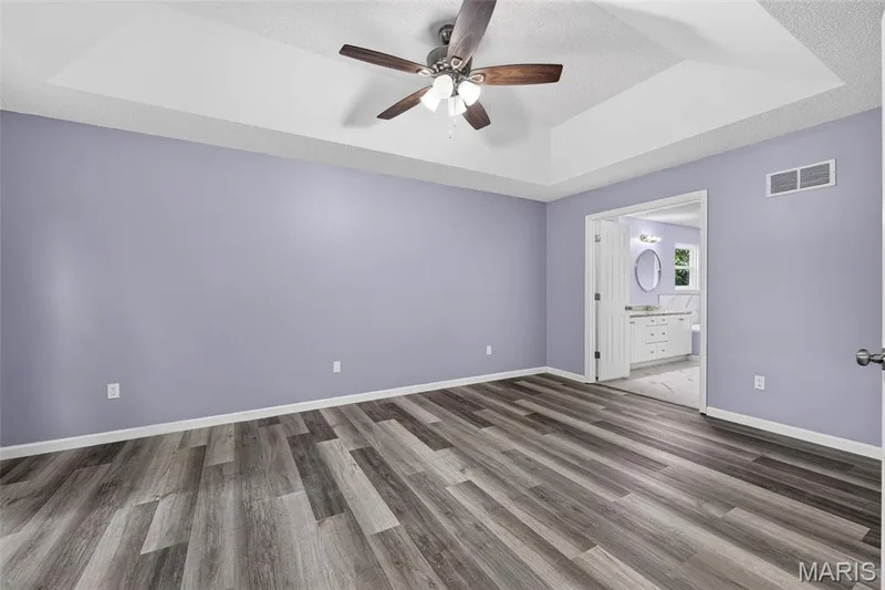 Spacious room featuring wood-finish flooring, a tray ceiling, and a ceiling fan — 2947 Bromley Drive, O'Fallon, MO 63368