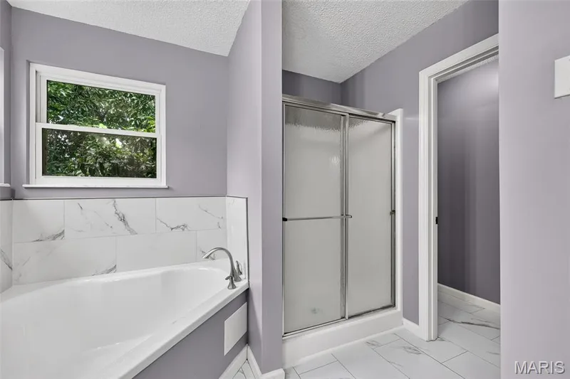 Bright bathroom featuring a built-in soaking tub with a brushed nickel faucet, a tiled surround, and a glass-enclosed shower with sliding doors — 2947 Bromley Drive, O'Fallon, MO 63368