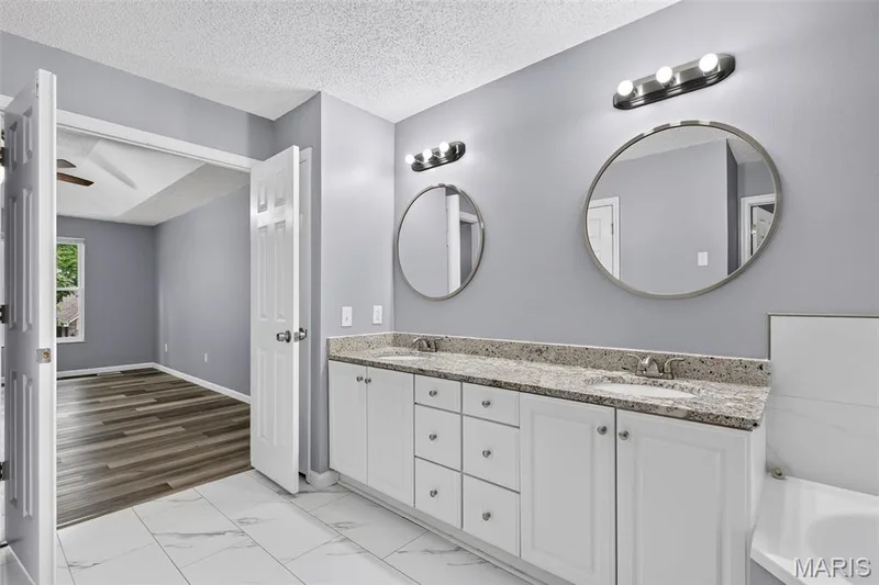 Dual vanity featuring white cabinetry, stone-finish countertop, and undermount sinks — 2947 Bromley Drive, O'Fallon, MO 63368