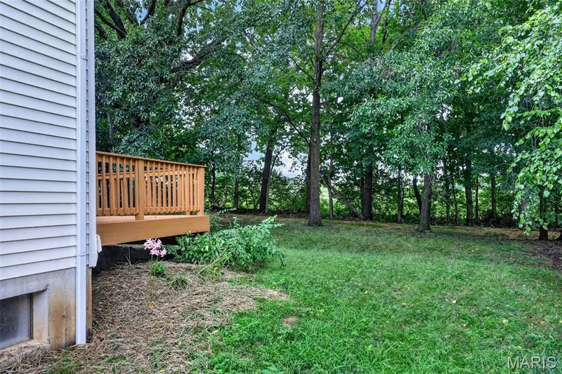 Rear exterior featuring a wood deck with wood railings, a white siding facade, a basement window, and a treed perimeter — 2947 Bromley Drive, O'Fallon, MO 63368