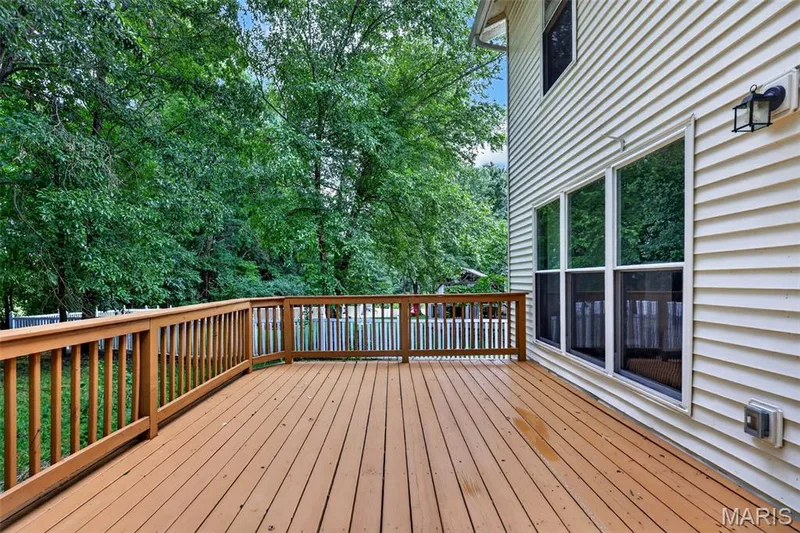 Spacious outdoor deck with natural wood-tone decking and railing, bordered by a white picket fence — 2947 Bromley Drive, O'Fallon, MO 63368