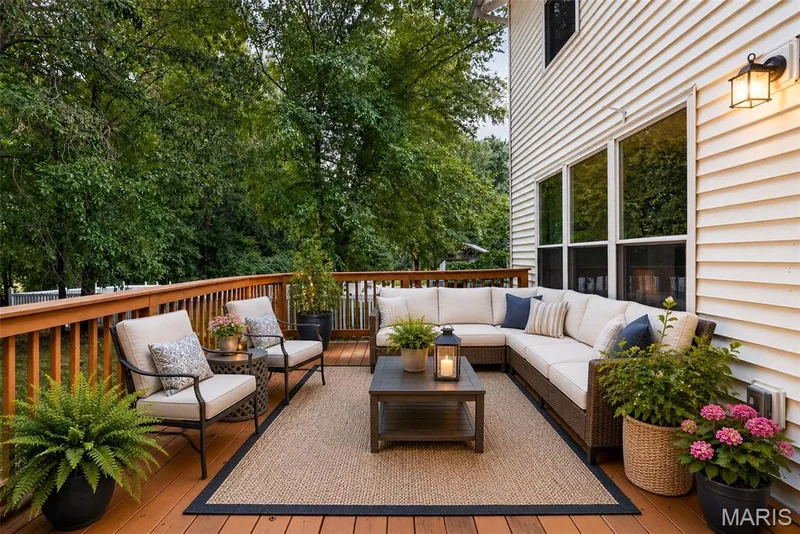 Spacious outdoor deck featuring wood-finish flooring and railing, a large area rug, multiple windows along the home's exterior, and a built-in outdoor light fixture — 2947 Bromley Drive, O'Fallon, MO 63368