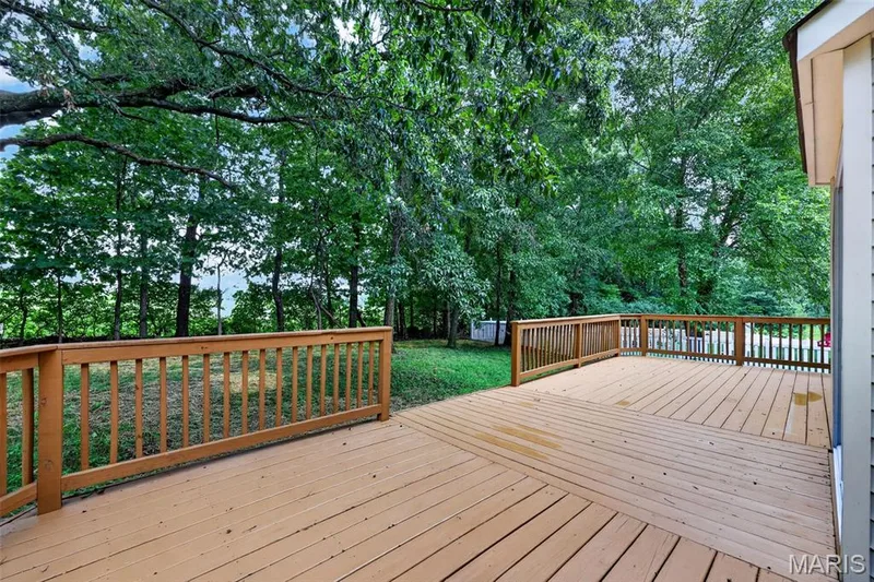 Spacious outdoor deck with natural wood railing overlooking a lush, treed backdrop and expansive lawn area — 2947 Bromley Drive, O'Fallon, MO 63368