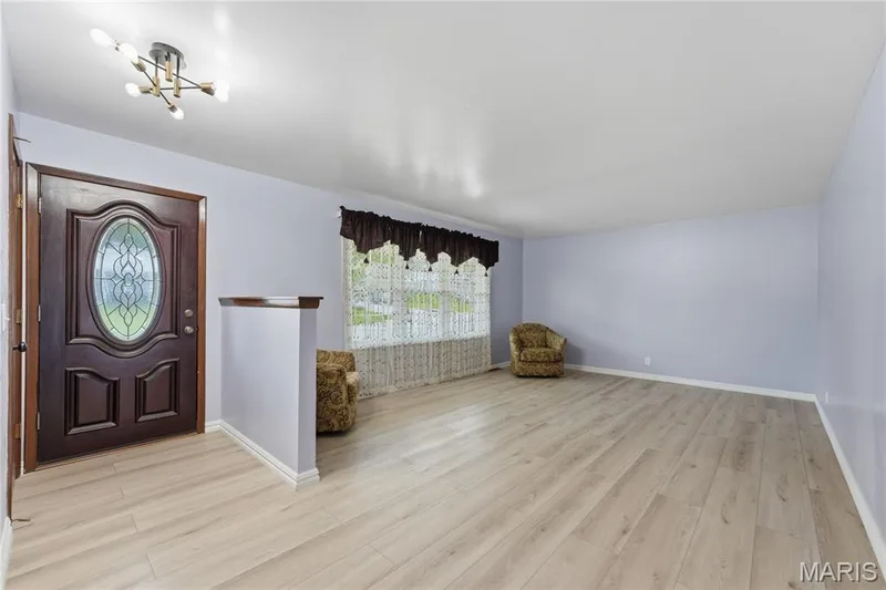 Entryway featuring a dark wood-finish door with an oval stained-glass insert, modern multi-bulb ceiling fixture, light wood-finish flooring, and light-toned walls — 1613 Tamarack Drive, St Charles, MO 63301