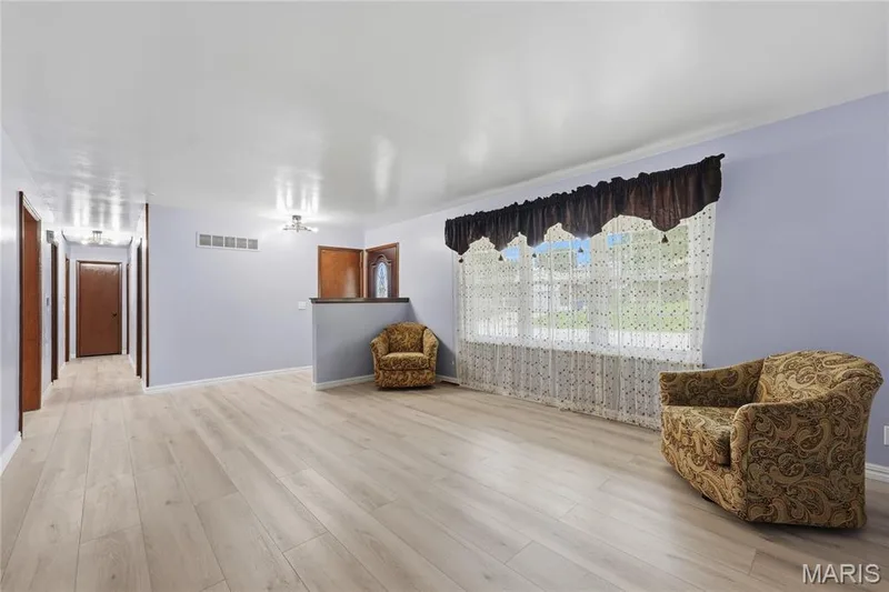 Spacious interior featuring light wood-finish flooring, a large window, and a hallway entrance — 1613 Tamarack Drive, St Charles, MO 63301