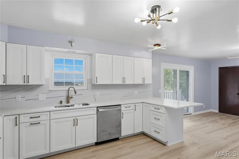 Kitchen featuring white cabinetry, light countertops, stainless steel sink, and a modern chandelier — 1613 Tamarack Drive, St Charles, MO 63301