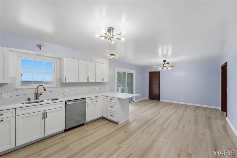 Modern kitchen featuring white cabinetry, light-toned wood-finish flooring, and a sliding glass door — 1613 Tamarack Drive, St Charles, MO 63301