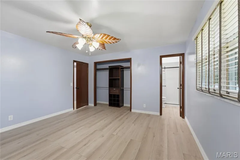 Spacious interior room featuring light wood-finish flooring, a ceiling fan with leaf-shaped blades, and light blue wall finishes — 1613 Tamarack Drive, St Charles, MO 63301
