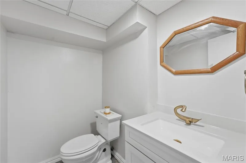 Half Bathroom featuring a white vanity with integrated sink, a brass-tone faucet, and an octagonal wood-framed mirror basement area — 1613 Tamarack Drive, St Charles, MO 63301