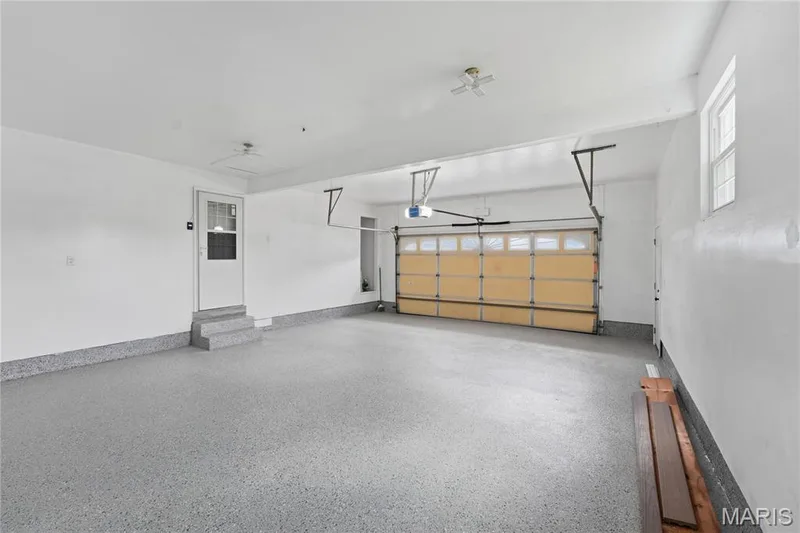 Spacious two-car garage featuring a light gray speckled epoxy floor, white painted walls, and a light wood-finish overhead door — 1613 Tamarack Drive, St Charles, MO 63301