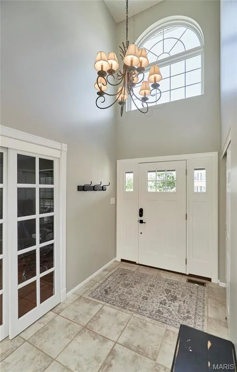 Two-story foyer featuring a prominent arched window, a decorative chandelier, white panel doors with glass inserts, and square tile flooring — 3 Floral Court, O'Fallon, MO 63368