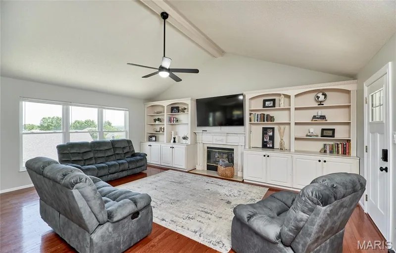 Living area featuring wood-finish flooring, a vaulted ceiling with exposed beams, and a ceiling fan — 3 Floral Court, O'Fallon, MO 63368