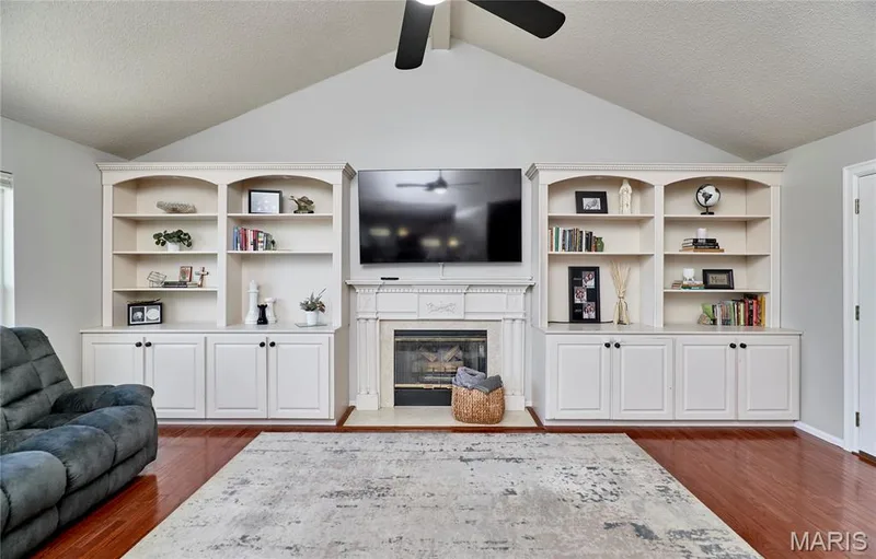 Spacious great room anchored by a custom built-in entertainment center featuring extensive shelving, display cabinetry with lower storage, and a centered fireplace with integrated TV mounting — 3 Floral Court, O'Fallon, MO 63368