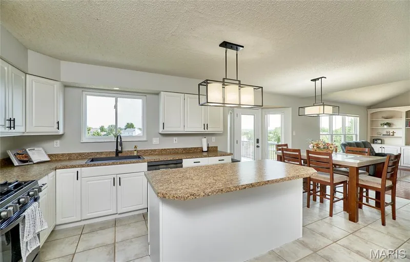 Kitchen featuring white cabinetry, speckled countertops, an island with seating, and tile flooring — 3 Floral Court, O'Fallon, MO 63368