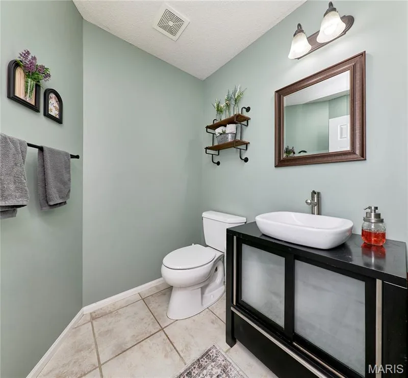 Powder room featuring a vessel sink, dark wood-finish vanity with frosted panels, and a framed mirror — 3 Floral Court, O'Fallon, MO 63368