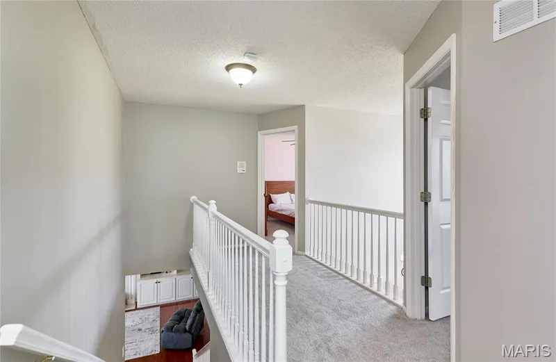 Upper-level hallway featuring a white spindle railing and neutral gray carpeting — 3 Floral Court, O'Fallon, MO 63368