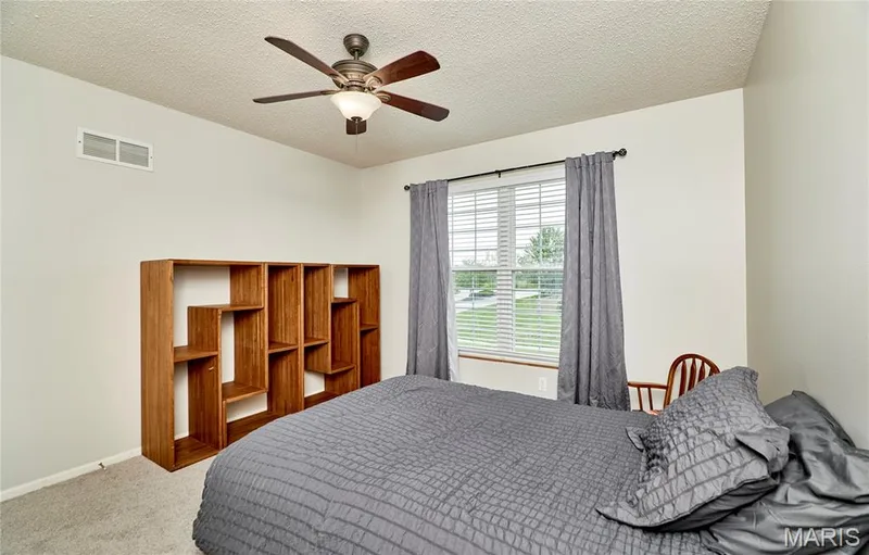 Room featuring a window with horizontal blinds, a ceiling fan with light fixture, and textured carpeting — 3 Floral Court, O'Fallon, MO 63368