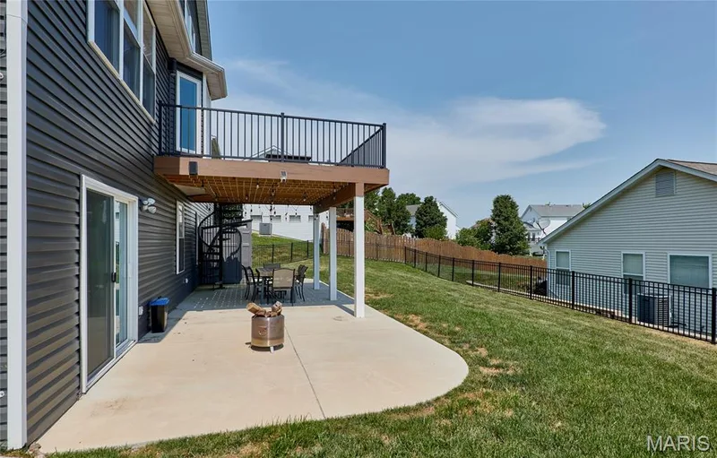 Expansive concrete patio beneath a raised deck featuring a spiral staircase — 3 Floral Court, O'Fallon, MO 63368