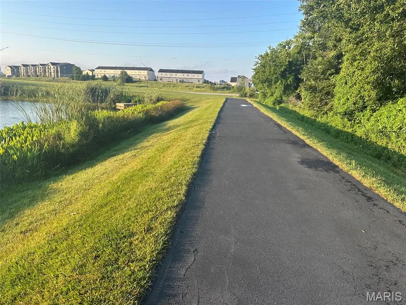 Paved pathway bordered by manicured lawn and mature foliage, featuring a tranquil pond — 110 Alta Mira Court, Dardenne Prairie, MO 63368