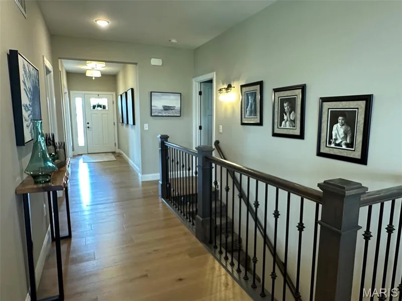 Hardwood flooring throughout a spacious hallway featuring a contemporary railing with black balusters and dark-stained newel posts — 110 Alta Mira Court, Dardenne Prairie, MO 63368