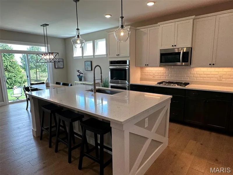 Spacious kitchen featuring a large island with seating, stainless steel appliances, two-tone cabinetry, subway tile backsplash, and wood-finish flooring — 110 Alta Mira Court, Dardenne Prairie, MO 63368