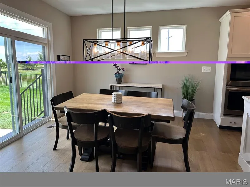 Dining area featuring wood-finish flooring, a modern linear chandelier, and a sliding glass door leading to the outdoor space — 110 Alta Mira Court, Dardenne Prairie, MO 63368
