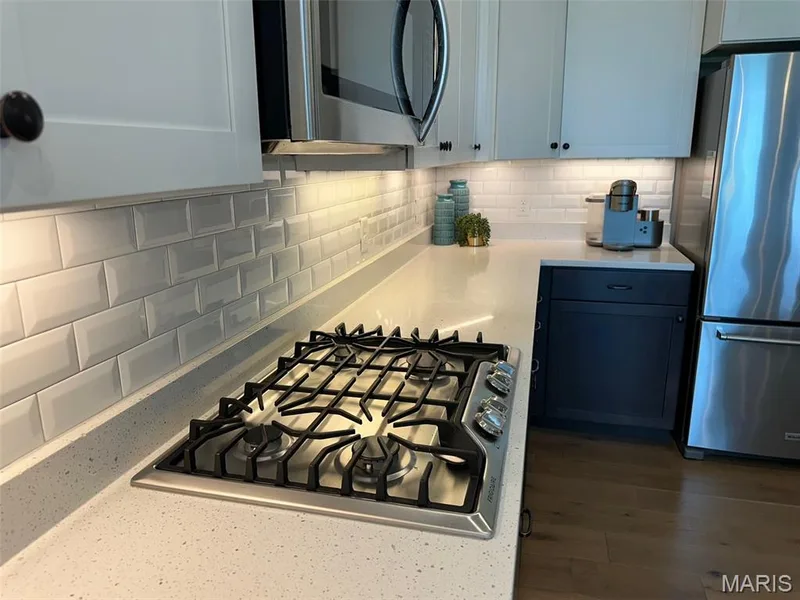 Kitchen featuring a built-in gas range, light-toned countertops, white subway tile backsplash, white upper cabinetry, and dark base cabinetry — 110 Alta Mira Court, Dardenne Prairie, MO 63368